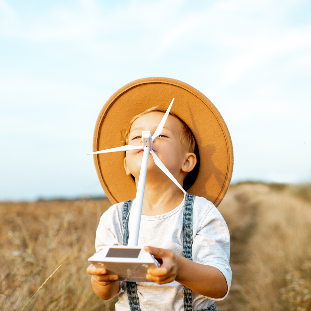 A kid in a field blowing on a toy wind turbine.