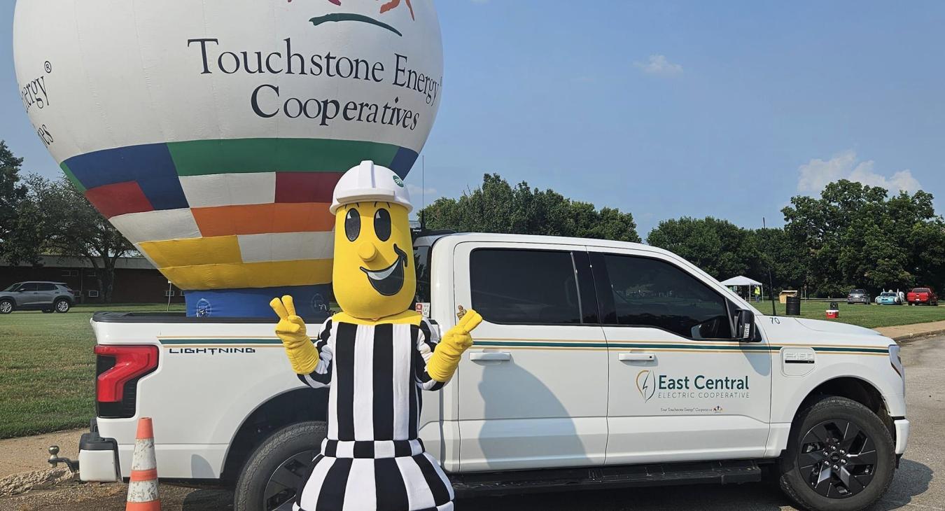 Willie Wiredhanc next to an East Central Electric branded Ford Lightning Truck, with a Touchstone Energy Cooperatives balloon in the bed. 